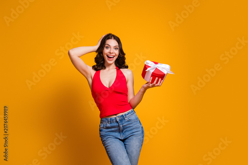 Fotografie Young woman in red top holding a wrapped gift and smiling with surprise on a bri