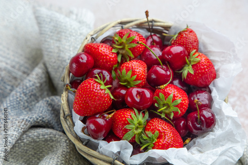Fresh strawberries and cherries in a woven basket on a light background in a kitchen setting