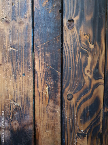 Texture of dark burnt wood with a clear pattern of annual rings, cracks, knots and screws. Vintage rustic wooden background