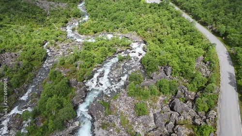 Aerial drone pan up of lower Trollstigen with flowing river and tree covered mountain walls, Norway