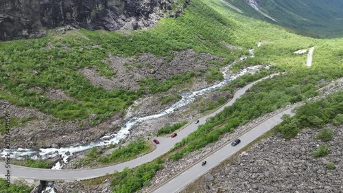 Aerial drone pan up of lower Trollstigen with flowing river and tree covered mountain walls, Norway