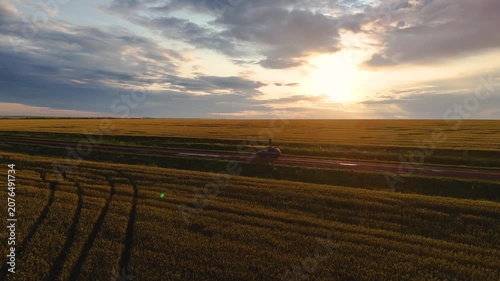 A young man stands on the roof of a car in a wheat field during the rain at sunset