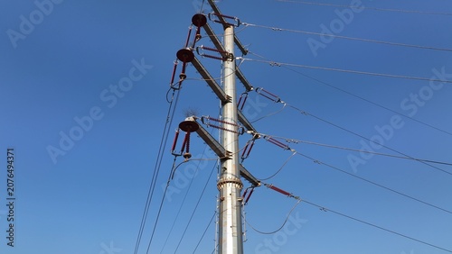 High voltage transmission tower with insulators and overhead power lines against clear blue sky