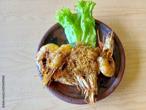 Fried prawns or served with spiced coconut flakes and lettuce garnish on clay plate. Indonesian traditional seafood dish culinary top view.