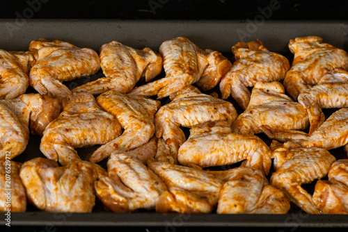 Raw chicken wings seasoned with spices arranged neatly on a baking tray ready for cooking in a kitchen setting with dark background