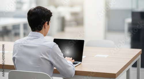 Professional working on a laptop in a modern office setting with large windows