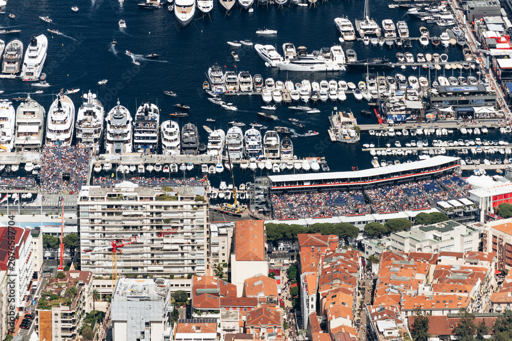 Obraz premium Monaco city center and Port Hercules during the Formula One Grand Prix with grandstands, luxury yachts and spectators viewed from Tete de Chien