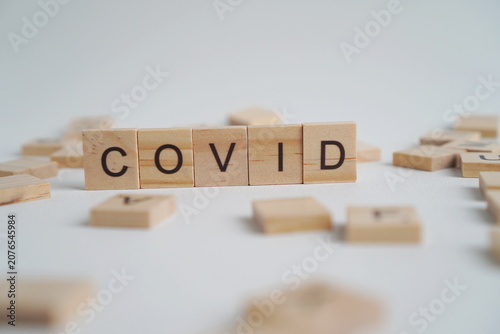 Photos The word COVID on a wooden block isolated on a white background with several wooden letter blocks as its border