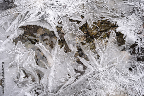 Obraz na plátně Close-up of intricate, sharp ice crystals frozen over a rocky riverbed in winter