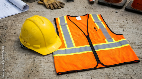 Yellow hard hat and orange safety vest on concrete floor background.