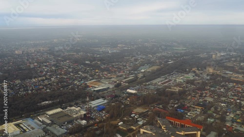 Cityscape and suburbs viewed from a descending airplane window during landing approach under a hazy overcast sky, real-time wide angle aerial shot.