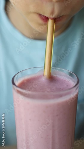 Close-up of a child drinking a pink strawberry milkshake