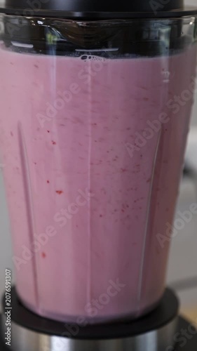 Swirling and mixing of strawberry and milk  in a glass blender for a healthy breakfast milkshake