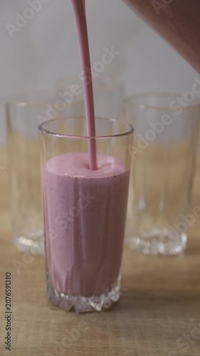 Pouring a pink strawberry milkshake into a glass