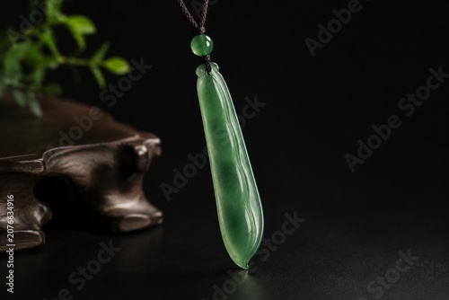 A slender green jade pendant shaped like a silique on a dark background.