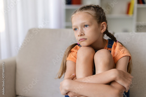 Canvas Print Pensive teen girl sitting alone on sofa at home hugging her knees, showing sadne
