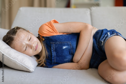 Foto Teen girl lying on sofa at home holding her stomach with eyes closed, showing ab