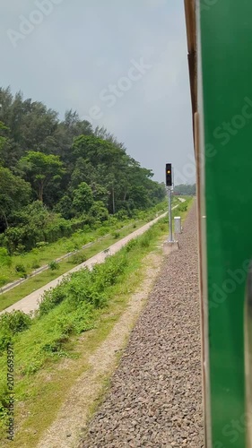 Green train window view moving along tracks past lush vegetation and trees on sunny day scenic journey rural landscape outdoor movement.