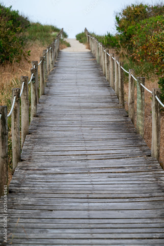 Fototapeta premium Rustic wooden footway with rope railing guiding towards sea shore
