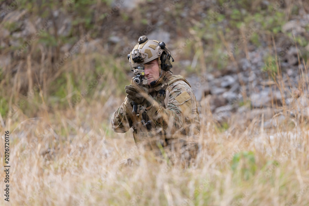 Fototapeta premium Soldier in military gear aims weapon while crouching in tall grass