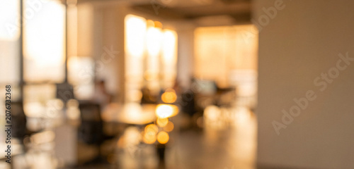 A soft-focus image of a modern office setting bathed in warm sunset light. The blurred background features workspaces and large windows.