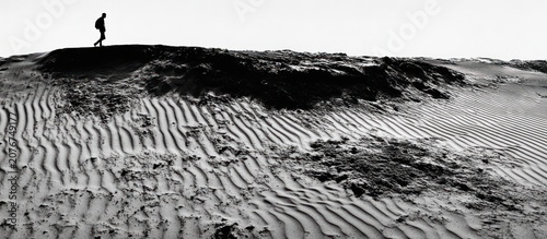 Solitary figure walking on a textured sand dune landscape.
