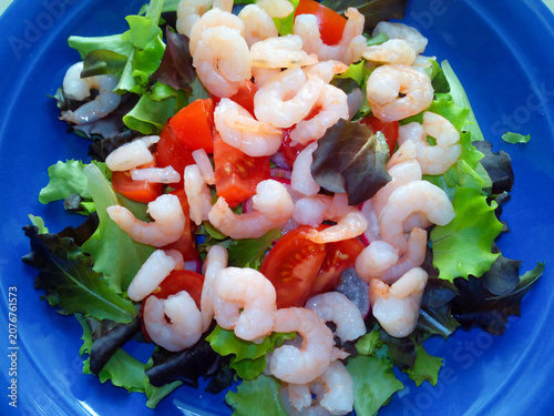 Fresh salad with shrimps, cherry tomatoes and mixed lettuce leaves on a blue plate.