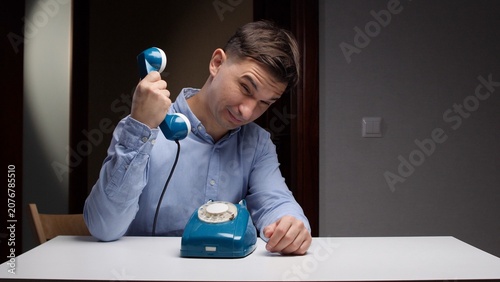 Foto Man in a light blue shirt sitting at a white desk, holding the receiver of a ret