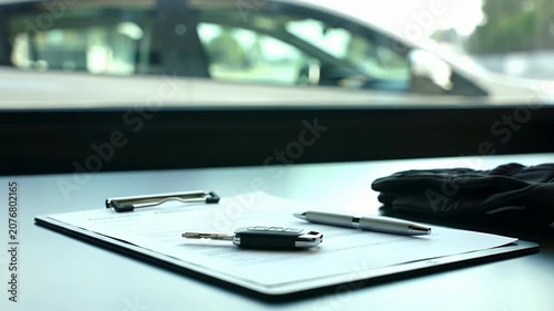 Close-Up Shot of Silver Car Key and Professional Instructor's Desk Setup with Gloves and Pens on Clipboard in a Modern Workplace