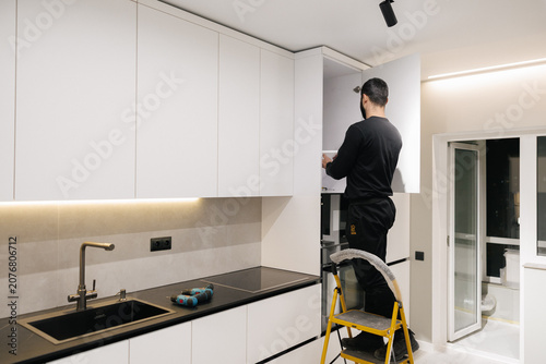 Photos Professional worker installing white custom kitchen cabinets in a modern residen