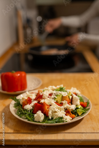 Fresh homemade vegetable salad with mozzarella cheese, avocado, tomatoes and red bell pepper served on plate, healthy balanced meal prepared in cozy kitchen with soft warm light