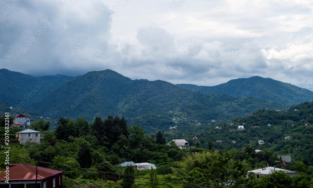 Obraz premium Rural house on a lush green hillside with a mountain village and blue sky in the background
