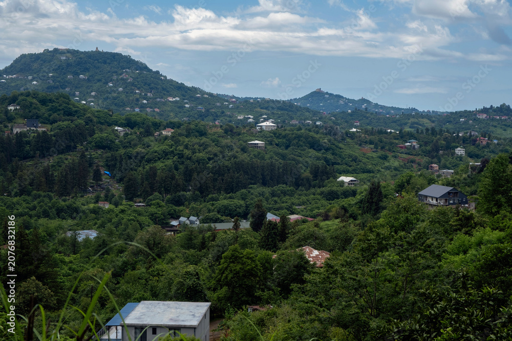 Obraz premium Rural house on a lush green hillside with a mountain village and blue sky in the background
