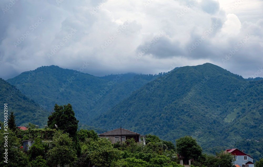 Obraz premium Mountain landscape under dramatic storm clouds with rural houses nestled in lush green hills