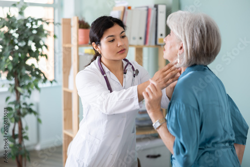 Fotografie Senior woman holds sore spot with hand, complains to female doctor, talks about deterioration of health