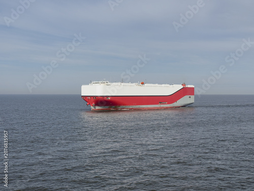 Massive RoRo car carrier ship sailing at full speed on the open sea. Huge vessel cuts through blue water leaving a wake. Powerful view of maritime transport and global vehicle logistics.