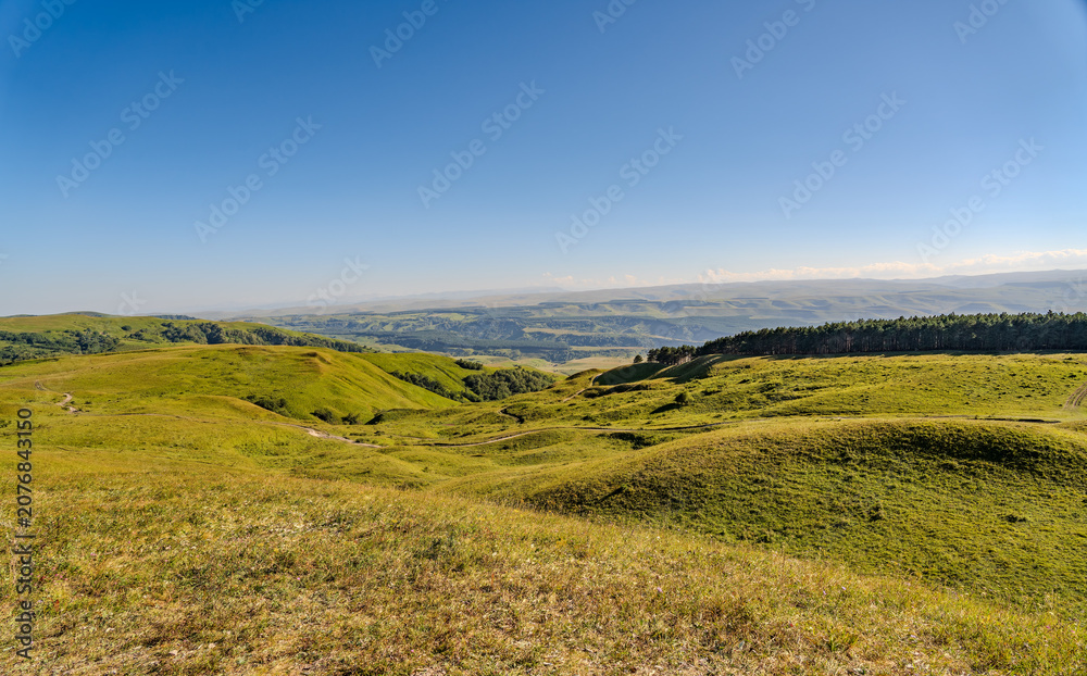 Fototapeta premium Layers of green mountains and hills in the haze during sunset. Panoramic View of Green hills and Meadow.