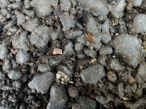 Close up of damaged black asphalt road surface with broken gravel stones and cracks showing rough construction material texture for background  