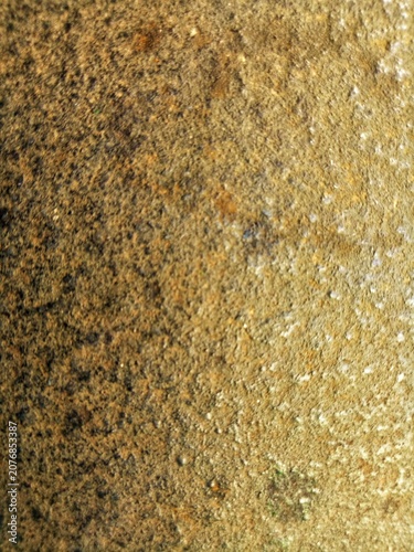 Close up of rough brown golden concrete surface with small stones and speckled pattern showing aged weathered industrial material texture background  