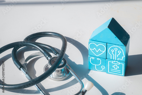 Stethoscope and blue wooden house blocks with medical icons on white background. Home healthcare, family medical insurance, and digital health technology building concept.