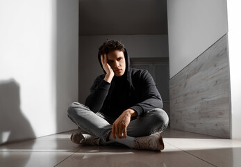Sad young man sitting on floor in hall. International Stress Awareness Week