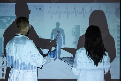 Young doctors analyzing scientific data on projector screen in laboratory, ba...