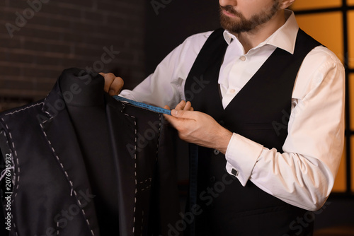 Male tailor measuring jacket on mannequin in atelier at night