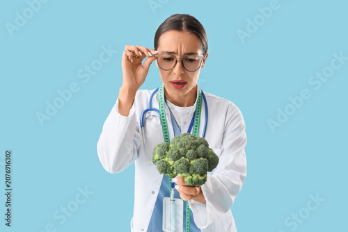 Thoughtful female nutritionist with broccoli on blue background
