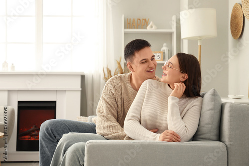 Cute young couple in warm sweaters hugging on sofa at home