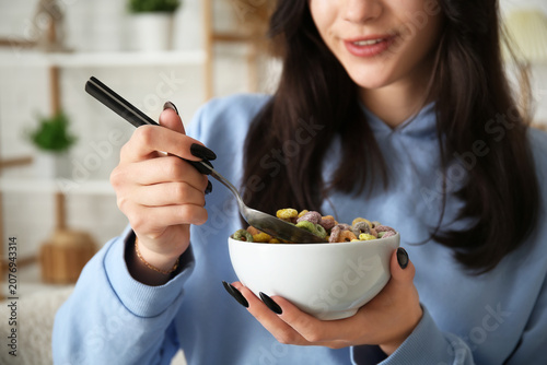 Young woman with bowl of tasty cereal rings at home, closeup