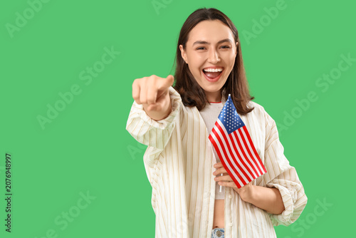 Bild auf Leinwand Laughing young woman with USA flag pointing at viewer on green background