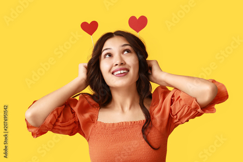 Beautiful young Asian woman with red paper hearts on yellow background. Valen...