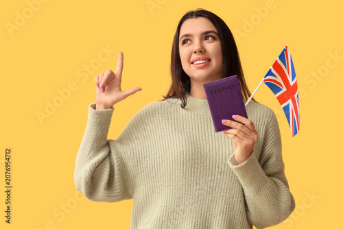 Beautiful young happy woman with UK flag and passport pointing at something o...