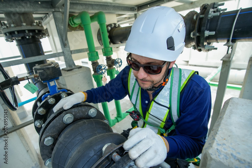 Engineer maintenance hvac cooling tower technician inspection industrial safety valve adjustment under hard hat and vest as worker checks pipe joint for reliable water flow on rooftop facility
